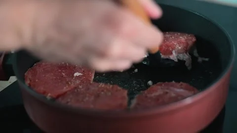 A person is using a spatula to flip meat patties in a frying pan on a heat Stockbeeldmateriaal 338304092