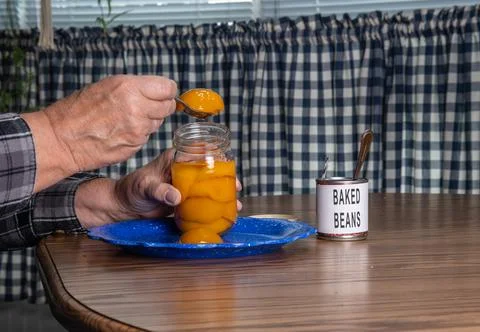 Person Using a Spoon to Serve Peaches From a Jar on a Table With Baked Bean.. 스톡 사진
