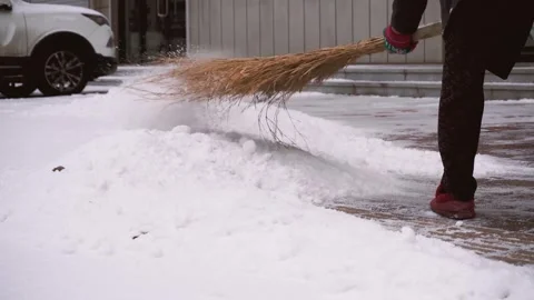 Person using a straw broom to clear fresh snow from a paved walkway Video stock 341949516