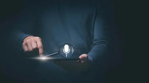 Person using tablet with microphone icon in dark setting Stock Photos
