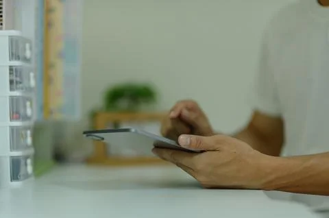 Person Using Tablet in Modern Office with Shelving and Green Plant in Backg.. Stock Photos
