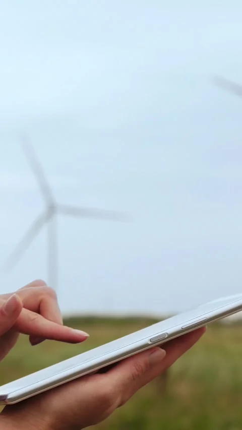 Person using tablet outdoors near wind turbines. Modern technology supports Stock Footage 343886085