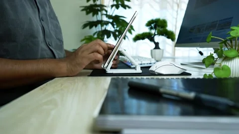 Person using a tablet on a stand at a modern workspace with plants Stock Footage 317737135