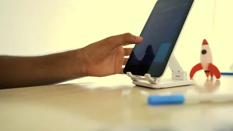 Person using a tablet on a stand with a toy rocket nearby Stock Footage 320725131