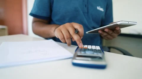 Person using a tablet while sitting at a desk, with a calculator and notepa.. Stock Footage 316799944
