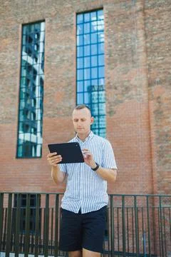 Person using a tablet while standing outside a brick building with large wi.. Stock Photos