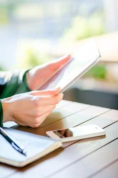 Person using a tablet at a wooden table with a notebook and smartphone in a Stock Photos