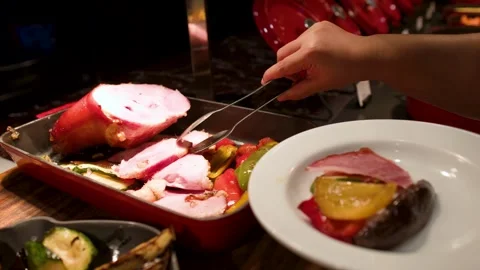 Person Using Tongs to Serve Roasted Ham and Vegetables at Buffet Stock Footage 334831828