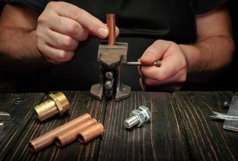 A person is using a tool to work on copper tubing and fittings on a wooden ta Stock Photos