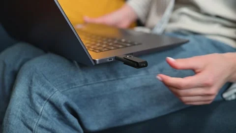 A person is using a USB drive to transfer data to a laptop while sitting on a Stock Footage 338446240