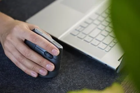 Person using vertical ergonomic mouse beside laptop on desk mat Foto stock