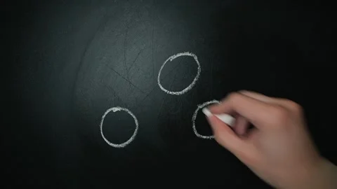 A person is using white chalk to draw several small circles on a dark chalkboard Stockbeeldmateriaal 338186438
