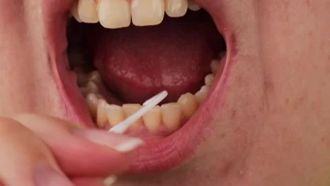 A person using a white dental floss pick to clean between lower teeth, Stock Footage 323331895