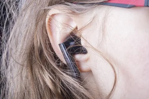 A person is using wireless earbuds to listen to music. Their hair partially c Stock Photos