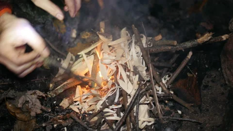 Person using wood chips to start a camp fire outdoors Stock Footage 153525975