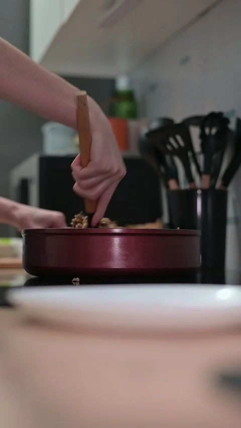A person is using a wooden spoon to stir ingredients in a pot on the stove. This Stockbeeldmateriaal 337112296