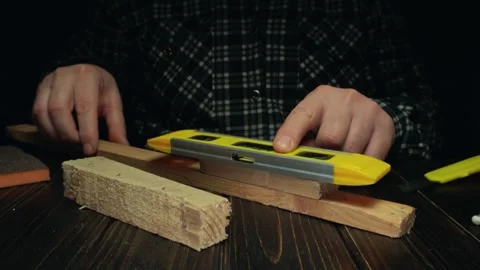 Person using a yellow level tool to measure wood pieces on a dark wooden table, Stock Footage 337163716
