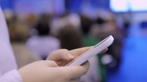 A person is utilizing their smartphone during a conference setting with focused Stock Footage 296732363