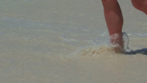 Person wading in shallow ocean waves at sandy beach shoreline Stock Footage 346369223