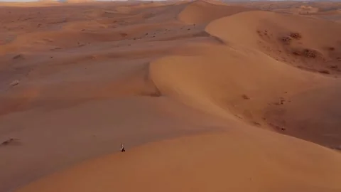 A person walking back on top of a dune, in golden sunset of a vast desert Stock Footage 131264368
