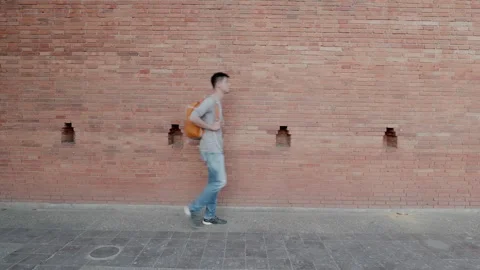 Person Walking by a Brick Wall with Backpack Stock Footage 314570137
