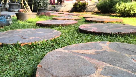 Person walking on round stone pathway in a lush green garden Stock Footage 340939147