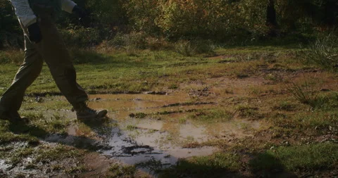 Person walking through a muddy puddle in the forest, splashing water with hiking Stock Footage 264933189