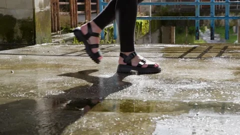Person walking through puddle in urban industrial area with blue metal railing Stock Footage 346799355
