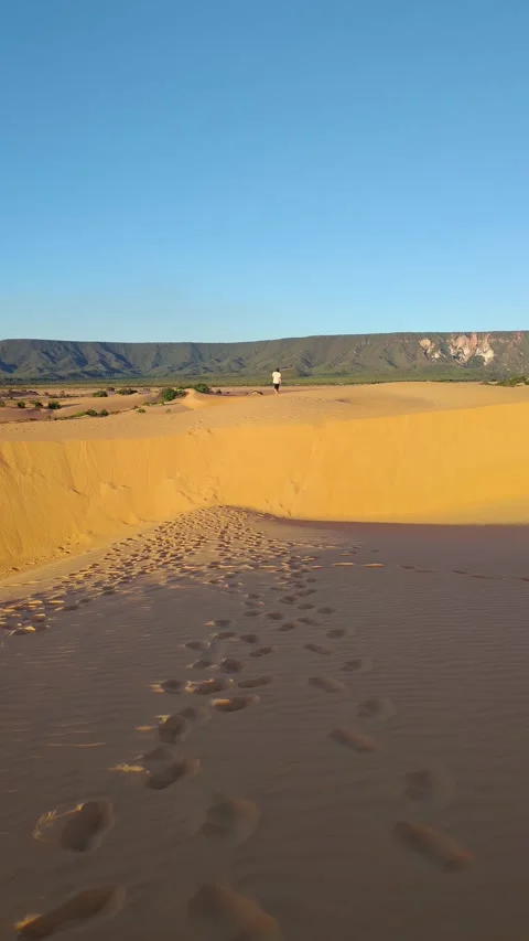 Person walking on a vast sand dune towards mountains at sunset. Stock Footage 312898103