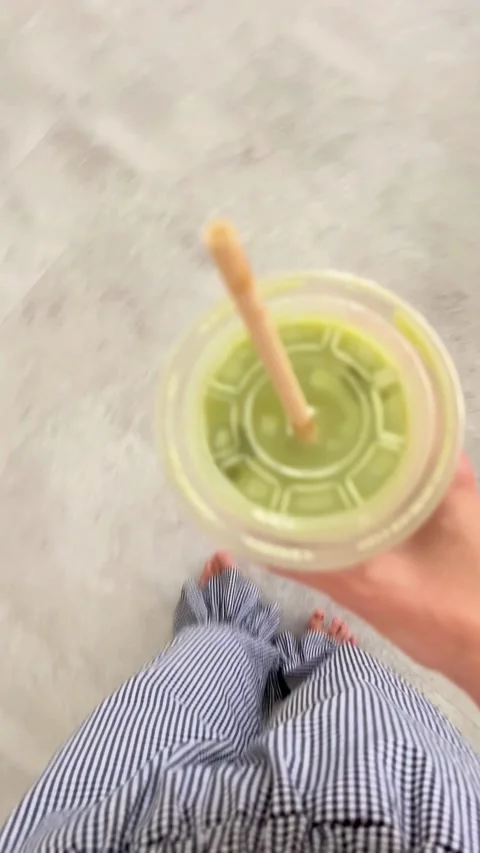 Person walking while holding a green matcha latte drink 스톡 동영상 331770697