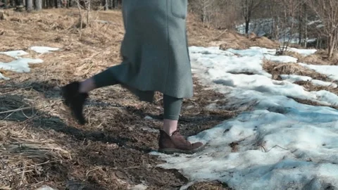 A person walks along a muddy path where snow is melting in a forest setting. The 库存影片 337642925
