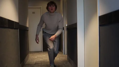 A person walks down a dimly lit hallway with a concerned or anxious expression,  Stock Footage 291551200