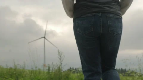 Person walks on grass looking at functioning windmill 動画素材 203973222