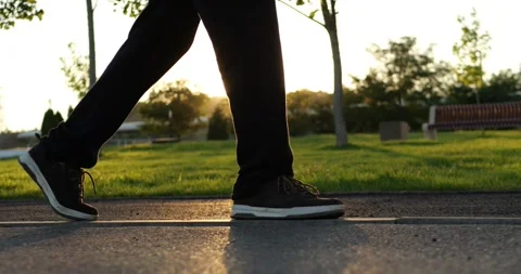 Person walks on park path in black sneakers at golden hour. Close-up footsteps Stock Footage 346753226