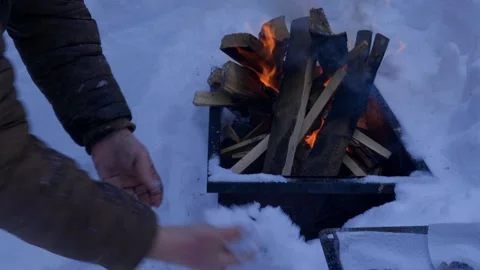 Person warming hands over burning fire in metal smoker box outdoors in deep snow Stock Footage 329579686