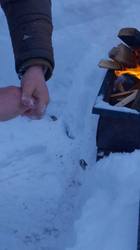 Person warming hands over burning fire in metal smoker box outdoors in deep snow Stock Footage 329581159