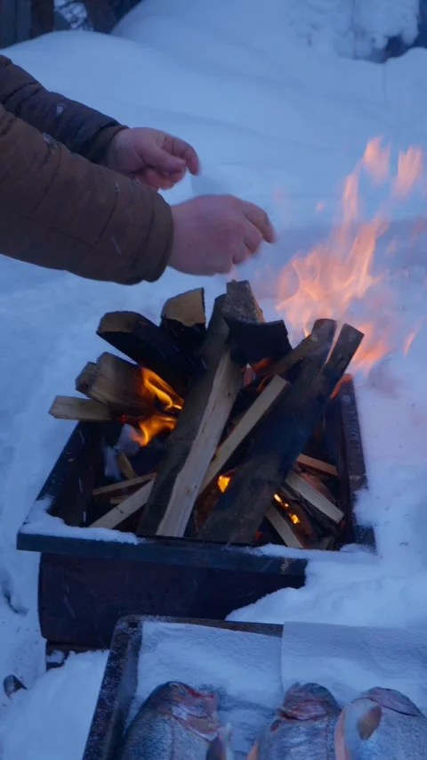 Person warming hands over burning fire in metal smoker box outdoors in deep snow Stock Footage 329581166