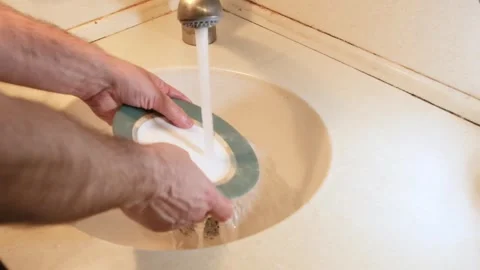 A person washes a plate with a sponge with detergent and rinses it with water Stock Footage 241111352