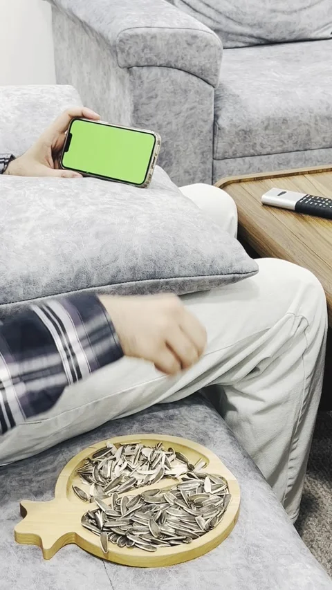 Person watching video on smartphone while eating sunflower seeds, vertical Stock Footage 345154123