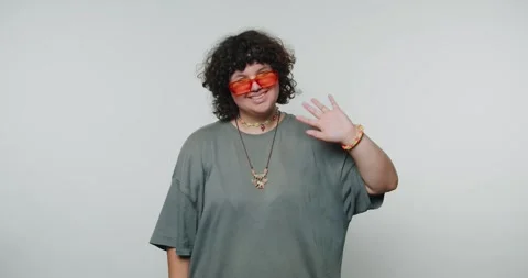 Person waves and smiles while wearing sunglasses inside a studio setting du.. Stock Footage 331990797
