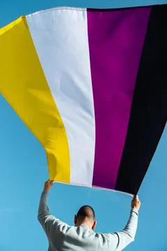 Person waves a non-binary pride flag outdoors Stock Photos