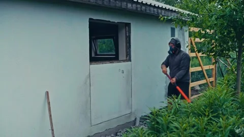 A Person is Wearing a Mask and Using a Tool to Break Through a Wall - Static Stock Footage 334023941