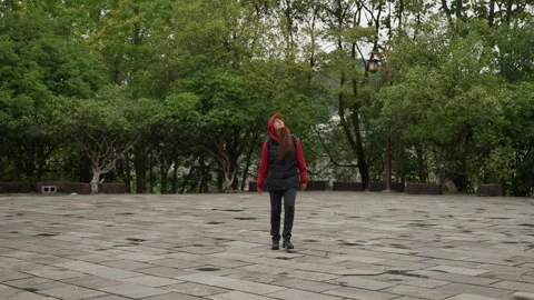 Person wearing red jacket walks alone through park. Lone individual in red coat Stock Footage 338076330