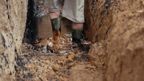 Person wearing rubber boots digging mud in trench Stock Footage 341294583