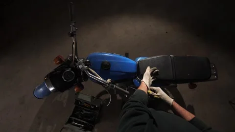 Person wearing work gloves maintaining a classic blue 1970s motorcycle, with a Stock Footage 342766144