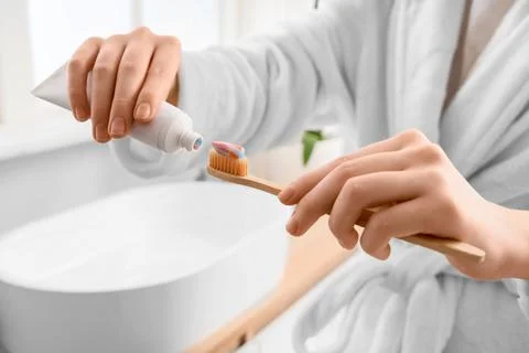 Person in white robe squeezing toothpaste onto eco-friendly bamboo toothbrush Фото