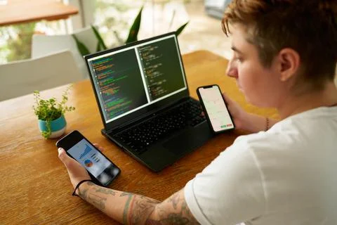 Person at wooden table multitasks with coding on laptop, analyzes data on two Stock Photos