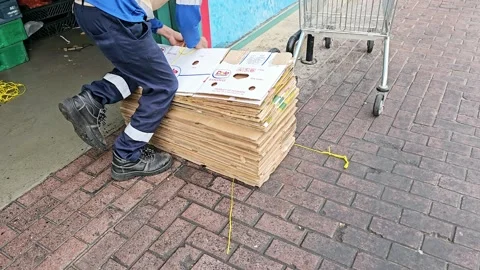 A person in work attire lifts a stack of cardboard boxes outdoors on a brick Stock-Footage 312002790
