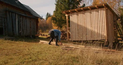 Person working on constructing a wooden structure outdoors near a log cabin. DIY Stock Footage 267126616