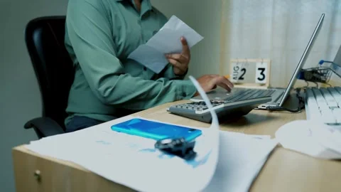 Person working at a desk with documents, calculator, and laptop Stock Footage 315982161